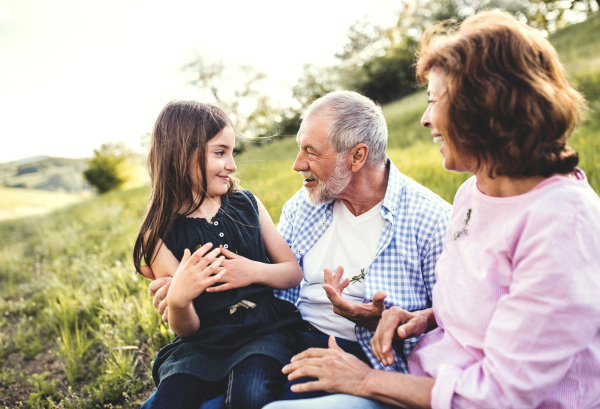 Senior couple with granddaughter outside in spring nature, relaxing on the grass and having fun.