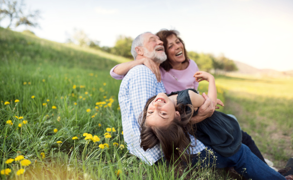 Senior couple with granddaughter outside in spring nature, relaxing on the grass and having fun.