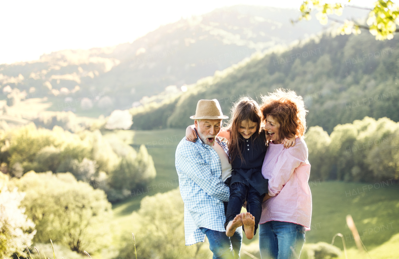 Cheerful senior couple with granddaughter outside in spring nature, relaxing and having fun.