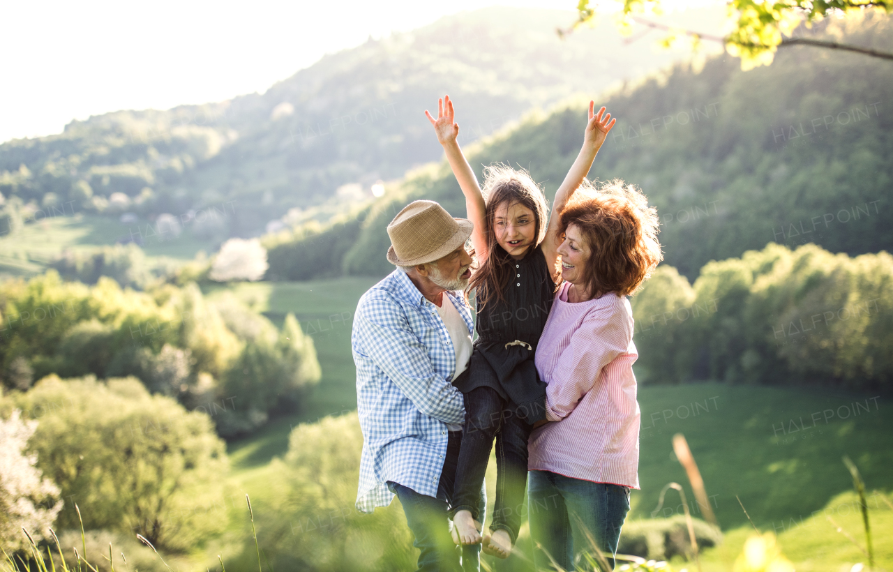 Senior couple holding their small happy granddaughter outside in spring nature.