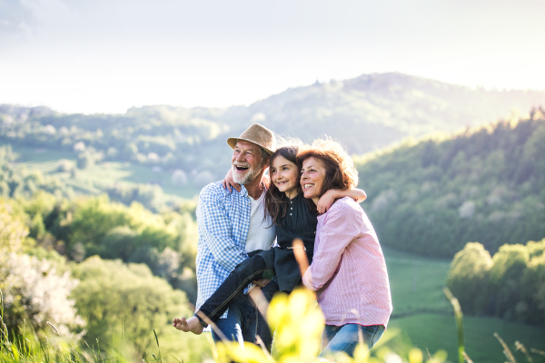 Cheerful senior couple with granddaughter outside in spring nature, relaxing and having fun.