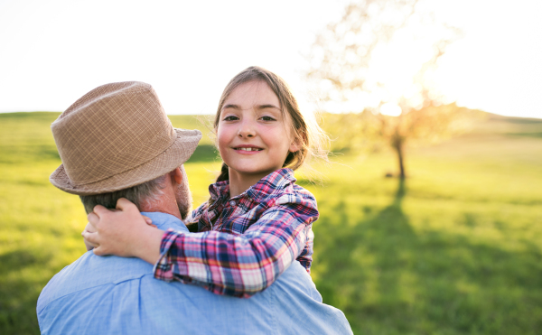 A cheerful small girl with grandfather outside in spring nature, having fun. Copy space.