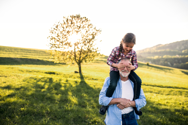 A senior grandfather giving a small granddaughter a piggyback ride. A girl covering mans eyes. Copy space.