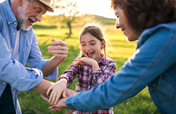 A happy small girl with her senior grandparents having fun outside. Sunset in spring nature.