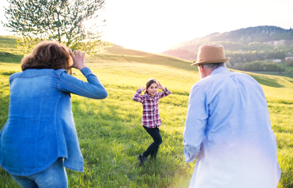 A happy small girl with her senior grandparents having fun outside in nature.