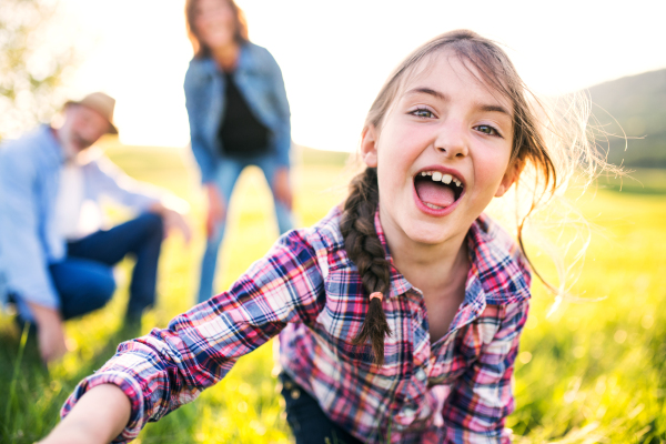 A happy small girl with her unrecognizable senior grandparents having fun outside in nature.