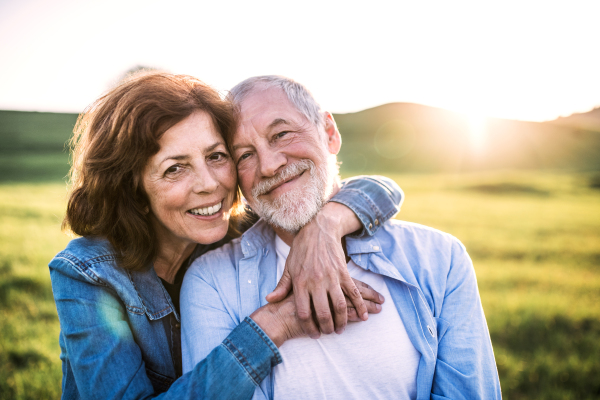 Happy senior couple outside in spring nature at sunset.