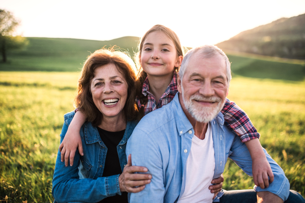 A portrait of senior couple with granddaughter outside in spring nature, relaxing on the grass.