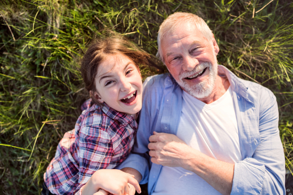 A small girl with grandfather outside in spring nature, relaxing on the grass. Top view.