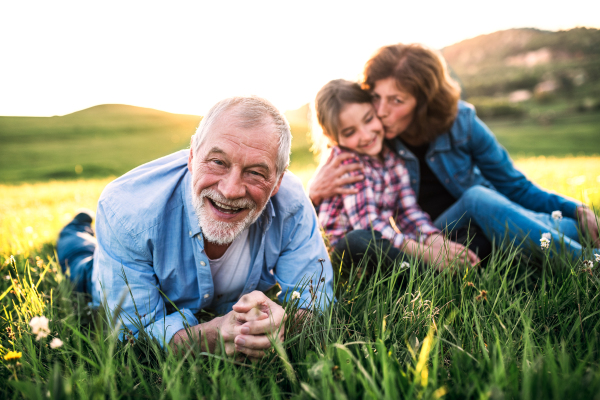 Senior couple with granddaughter outside in spring nature, lying on the grass and relaxing.