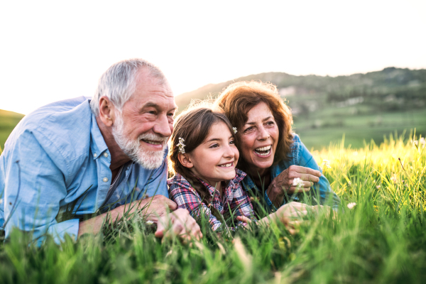 Senior couple with granddaughter outside in spring nature, lying on the grass and relaxing.