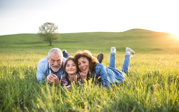 Senior couple with granddaughter outside in spring nature, lying on the grass and relaxing.