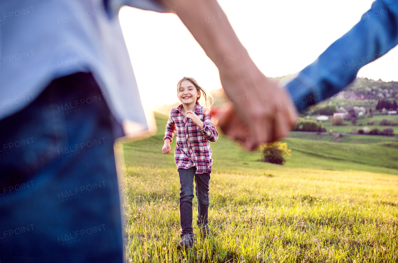 A happy small girl with her unrecognizable senior grandparents having fun outside in nature.