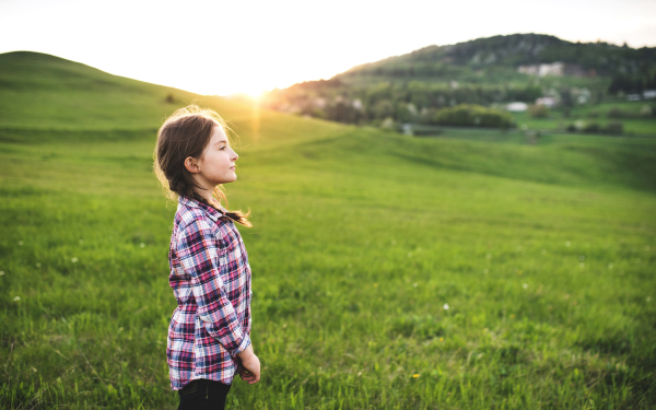 A happy small girl standing outside in nature. Copy space.