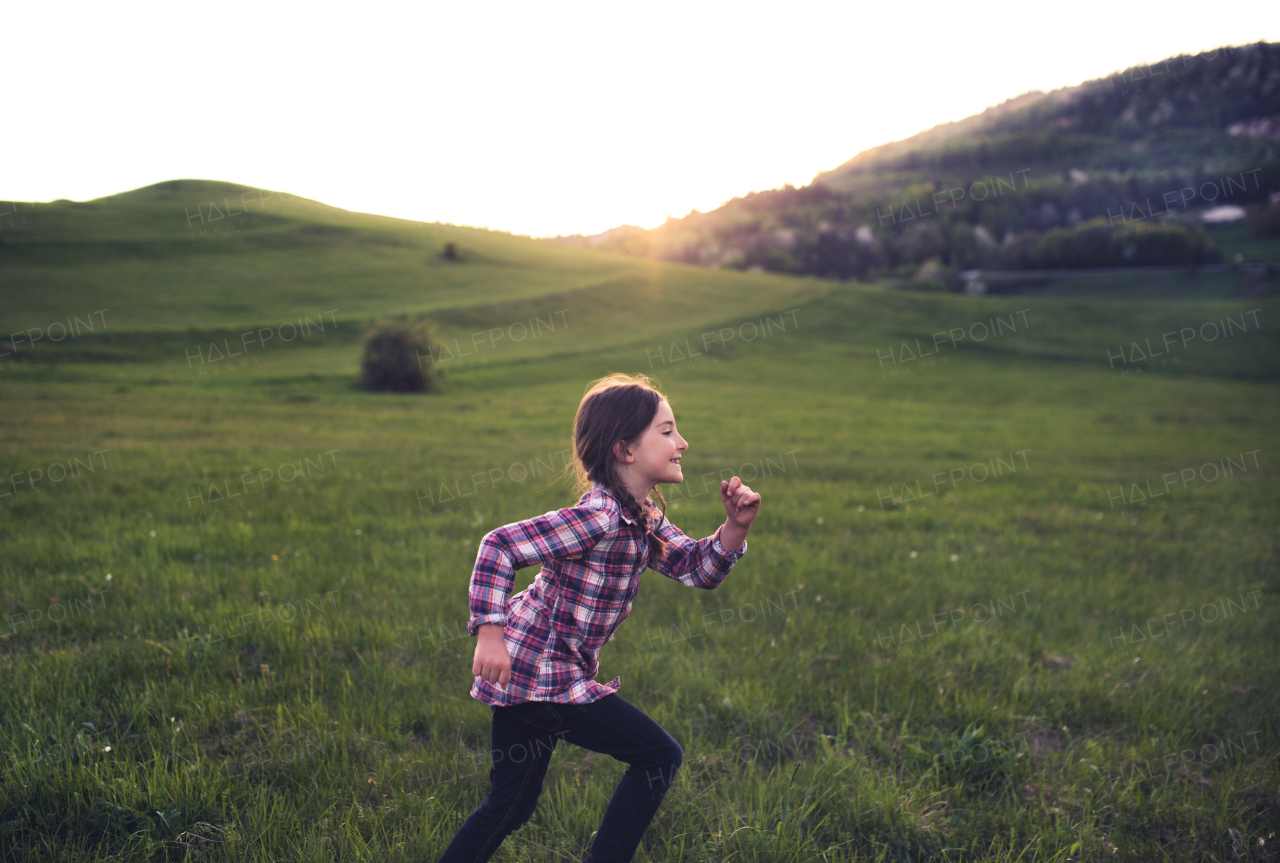 A happy small girl running outside in nature at sunset. Copy space.