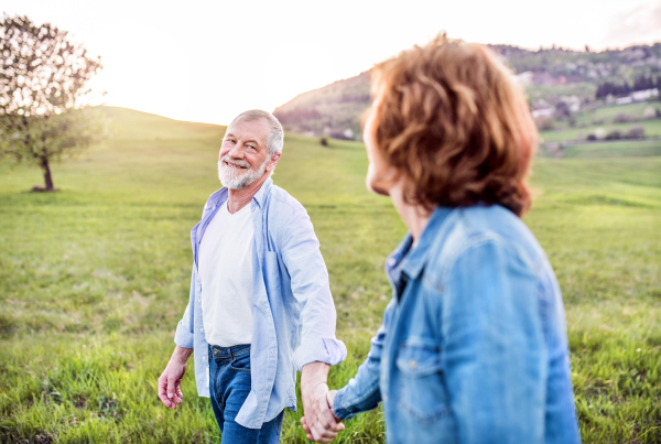 Happy senior couple walking outside in spring nature, holding hands.