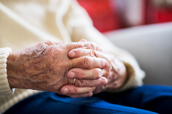 A close-up of a senior woman sitting and praying at home, hands clasped.