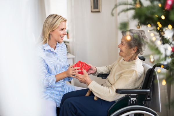 A health visitor and a senior woman in wheelchair with a present at home at Christmas time.