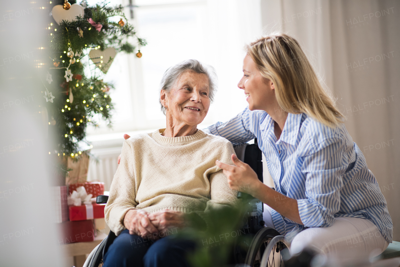 A senior woman in wheelchair with a health visitor at home at Christmas time, talking.