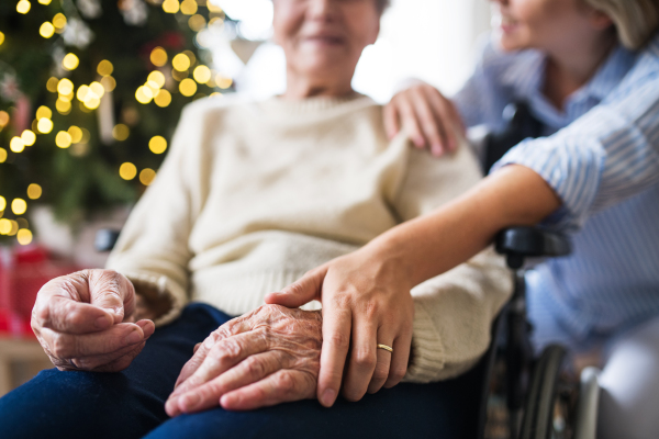 Unrecognizable senior woman in wheelchair with a health visitor at home at Christmas time.