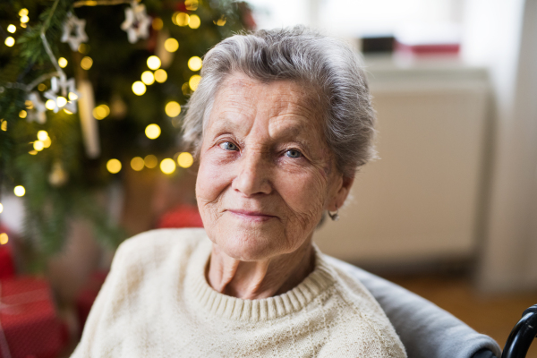 A portrait of a lonely senior woman in wheelchair at home at Christmas time.