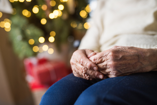 A close-up of hands and knees of an unrecognizable lonely senior woman sitting on an armchair at home at Christmas time.