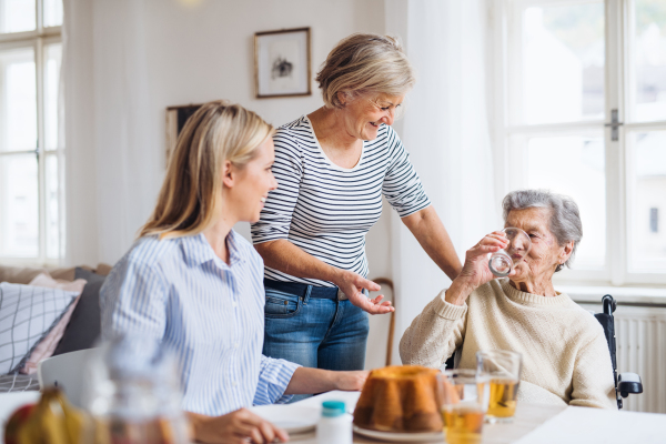 A happy senior woman in wheelchair with family sitting at the table at home, drinking.