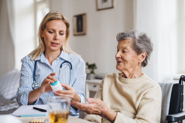 A young health visitor explaining a senior woman in wheelchair how to take medicine and pills.