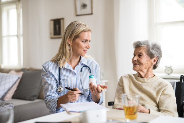 A young health visitor explaining a senior woman in wheelchair how to take medicine and pills.