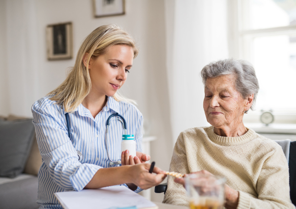 A young health visitor explaining a senior woman in wheelchair how to take medicine and pills.