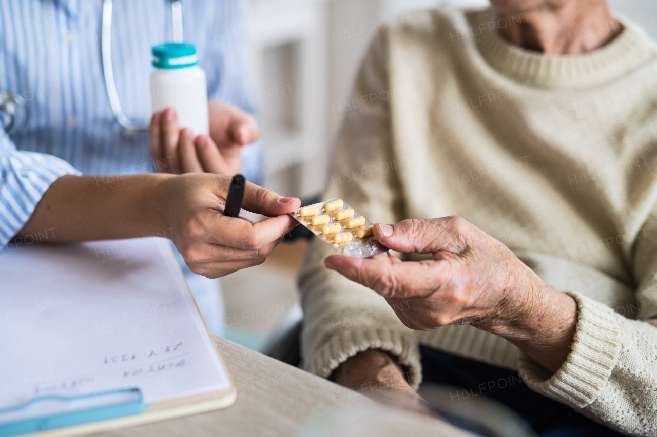 An unrecognizable young health visitor explaining a senior woman in wheelchair how to take medicine and pills.