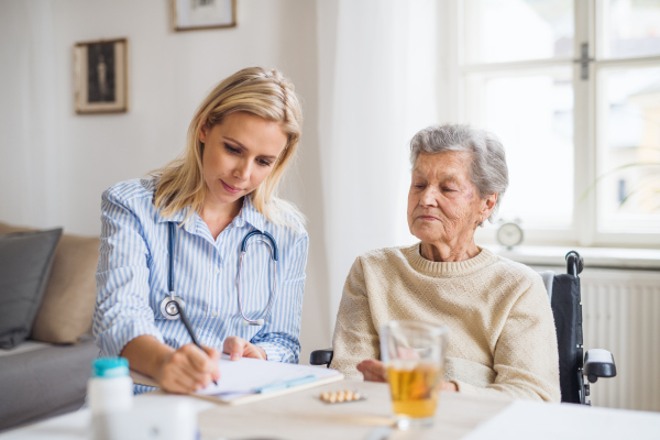 A young health visitor explaining a senior woman in wheelchair how to take medicine and pills.