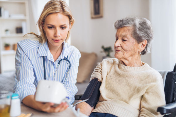 A young health visitor measuring a blood pressure of a senior woman in wheelchair at home.