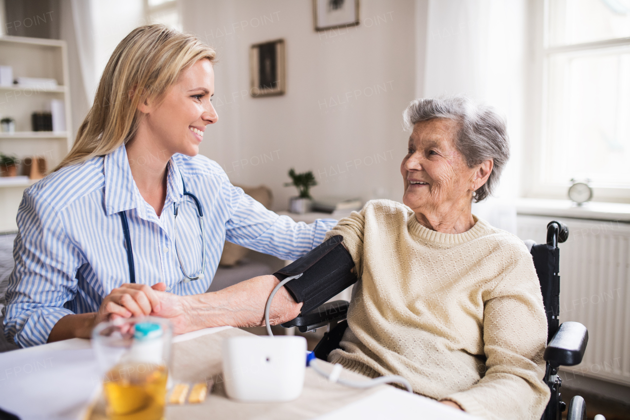 A young health visitor measuring a blood pressure of a senior woman in wheelchair at home.