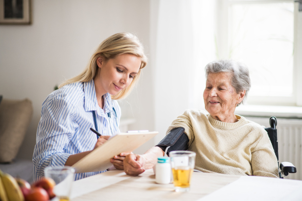 A young health visitor measuring a blood pressure of a senior woman in wheelchair at home.