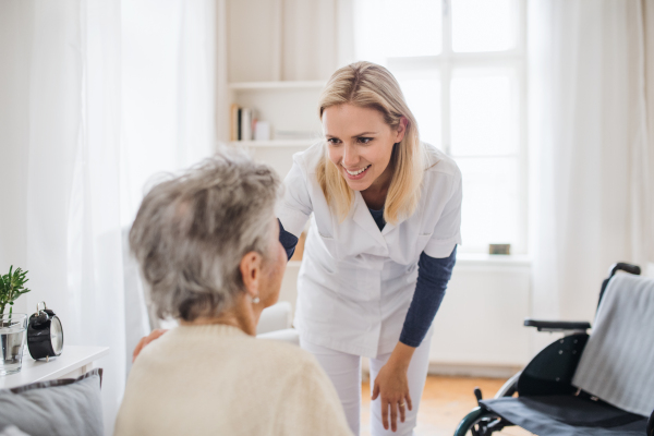 A health visitor talking to an unrecognizable senior woman sitting on bed at home.