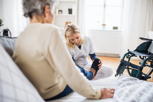 A young health visitor putting on slippers on a senior woman at home.