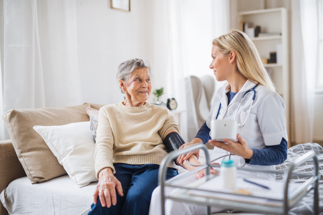 A young health visitor measuring a blood pressure of a senior woman at home.