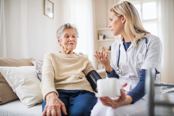 A young health visitor measuring a blood pressure of a senior woman at home.