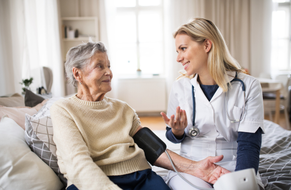 A young health visitor measuring a blood pressure of a senior woman at home.