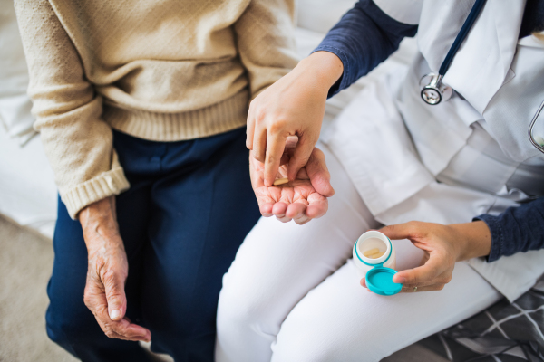 An unrecognizable young health visitor explaining a senior woman how to take medicine and pills. Midsection.