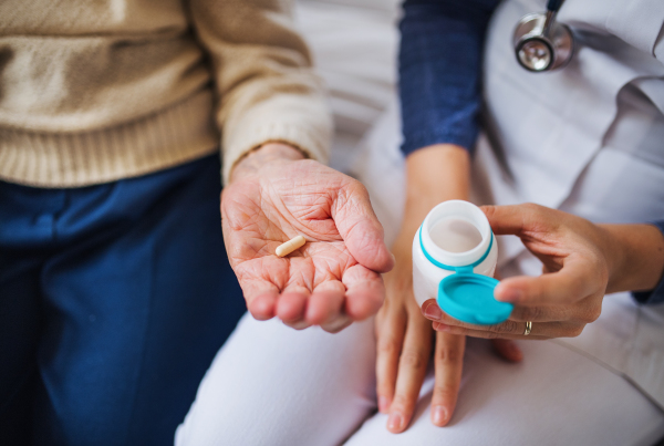 An unrecognizable young health visitor explaining a senior woman how to take medicine and pills. Midsection.