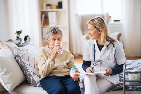 A young health visitor and a senior woman at home, taking pills.