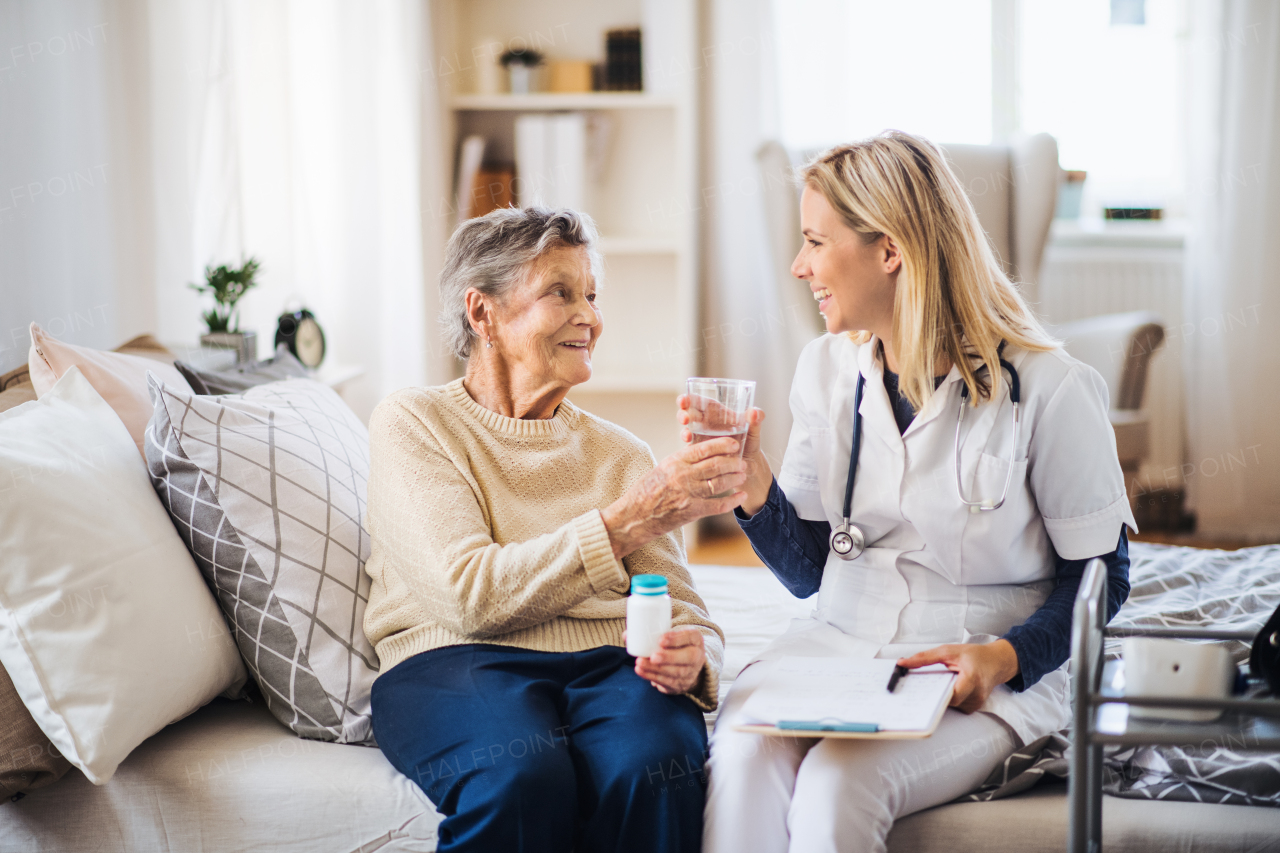 A health visitor giving a senior woman a glass of water, explaining her how to take pills.