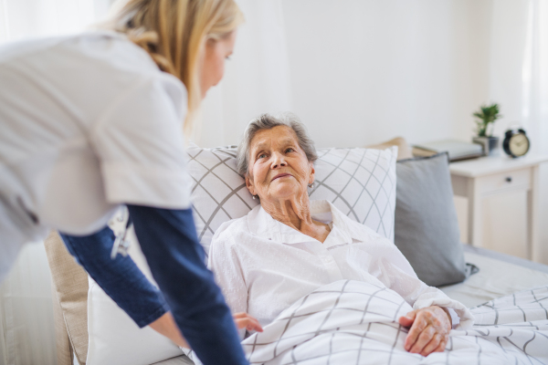 A young health visitor talking to a happy sick senior woman lying in bed at home.