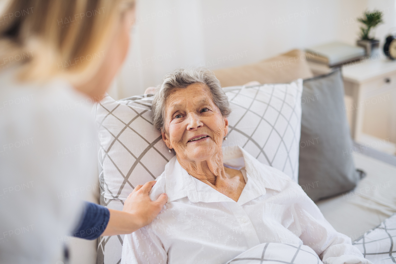 A young health visitor talking to a happy sick senior woman lying in bed at home.