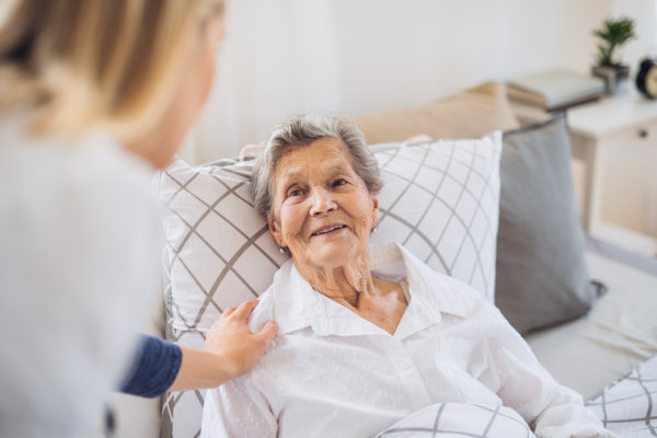 A young health visitor talking to a happy sick senior woman lying in bed at home.