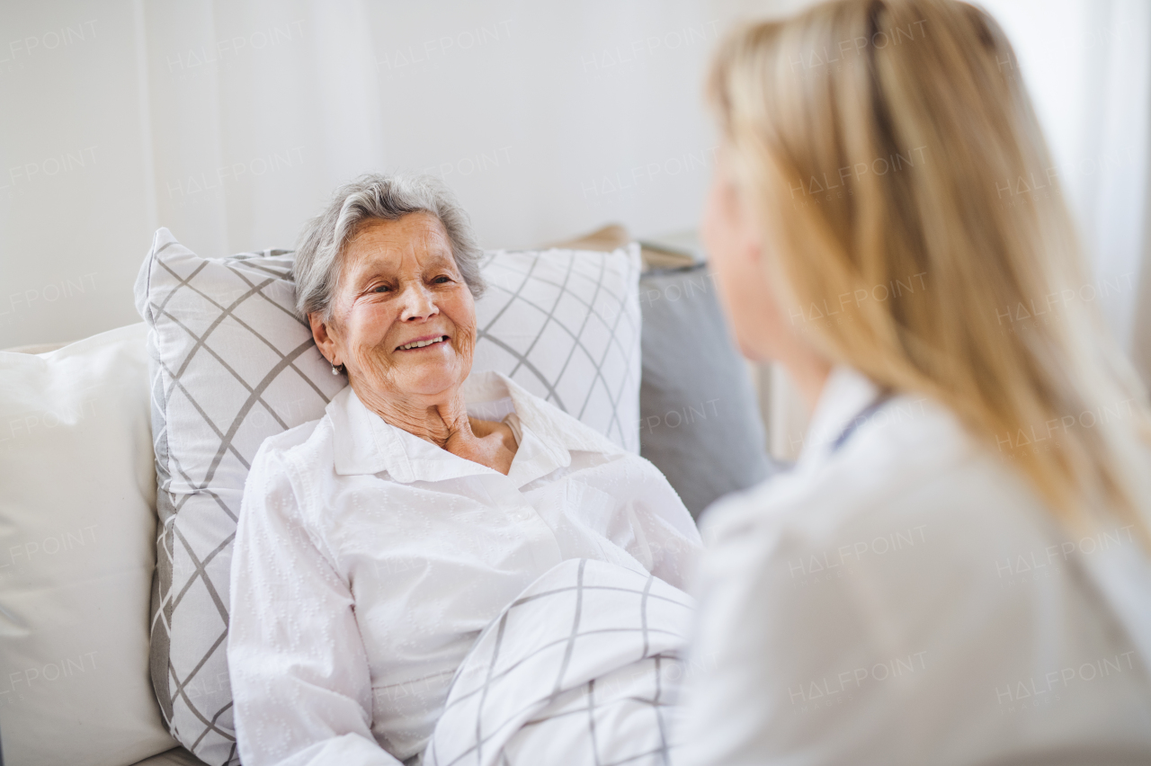 A young health visitor talking to a happy sick senior woman lying in bed at home.