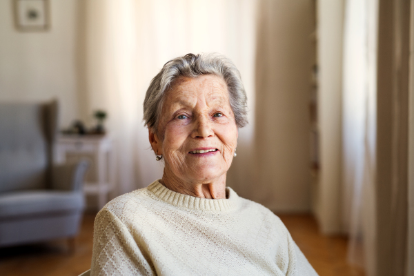 A portrait of a senior woman sitting on a chair at home, looking at camera.