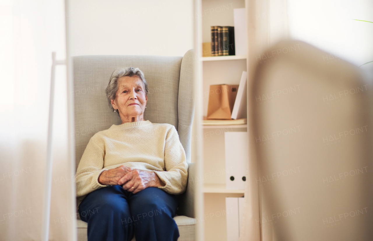 A portrait of a senior woman sitting on an armchair at home, looking at camera. Copy space.